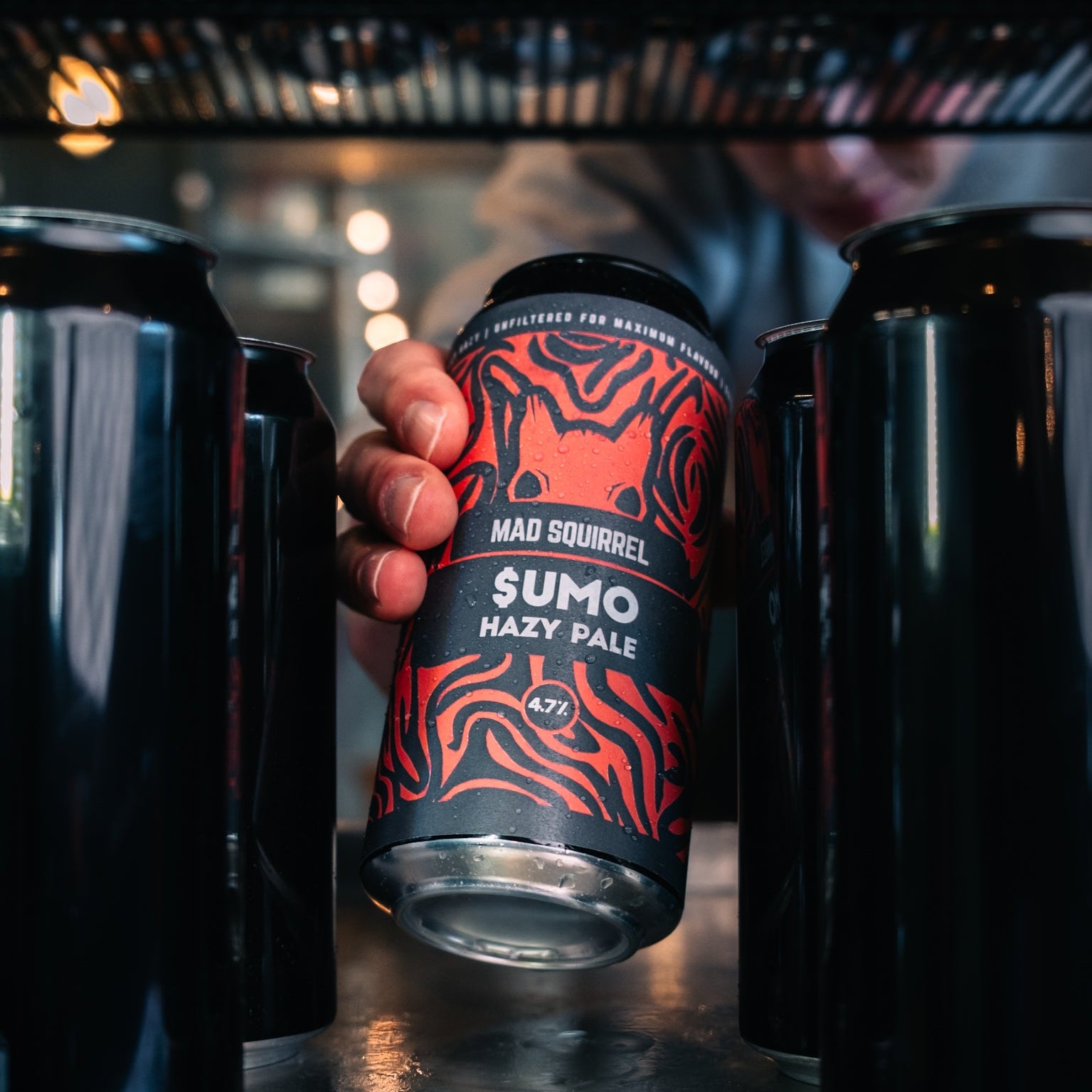 Person holding a can of Mad Squirrel Sumo Hazy Pale Ale with other cans in the background.
